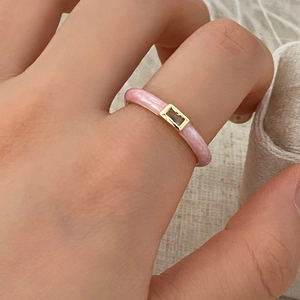 Primer plano detallado de un anillo de esmalte rosa con incrustación dorada al dedo