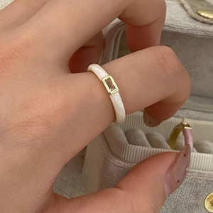 Detalle de anillo de esmalte crema con engaste dorado y piedra de circón transparente