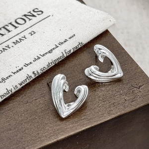 Macro shot of silver layered heart earrings with textured metallic finish on wood stand