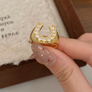 Close-up of a horseshoe-shaped gold ring with pavé-set zircons on a model's finger