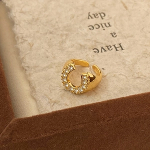 Golden horseshoe open ring with micro-paved zircons on a textured cream background