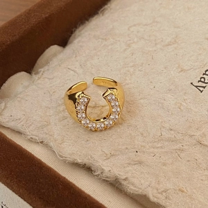 Macro view of gold horseshoe ring with white zircons on a textured cream background