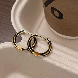 Detail of gold-plated hoop earrings with black enamel inlay on a cream texture tray