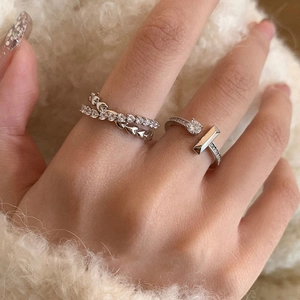 Detail of silver heart ring and zircon-set open ring worn on fingers with soft background
