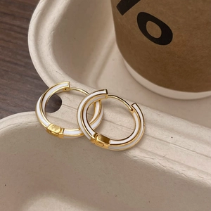 Detail of gold-plated hoop earrings with white enamel inlay on a beige display tray