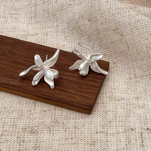 Macro shot of matte silver flower earrings with textured petals on a wooden background