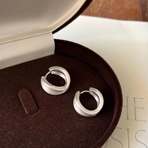 Macro shot of silver brushed metal hoop earrings in a dark brown velvet jewelry box