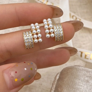 Close-up of elegant pearl and zircon stud earrings held by hand showing exquisite details