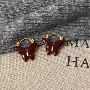 Detailed shot of vintage gold butterfly hoop earrings with deep burgundy enamel on fabric