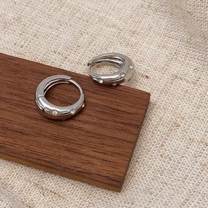 Macro shot of silver-colored huggie hoops with micro-set zircons on a wooden display