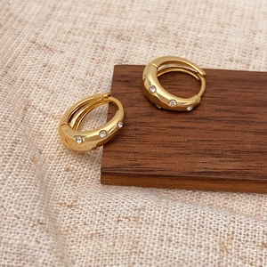 Macro shot of gold wide huggie earrings with micro-inlaid cubic zirconia on wooden stand