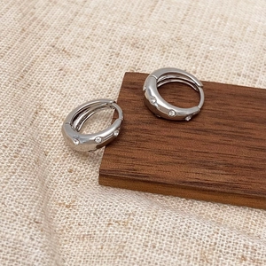 Macro detail of silver-toned hoop earrings with micro-inlaid cubic zirconia on wooden block