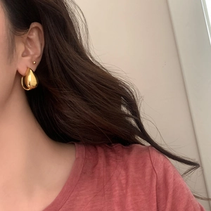 Close-up of a model wearing high-polished gold teardrop earrings in a minimalist style
