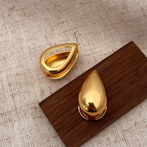 Detailed view of glossy gold teardrop earrings on wood and linen textured background