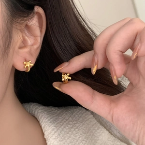Detailed close-up of delicate gold bow earrings showing size and polished finish on model