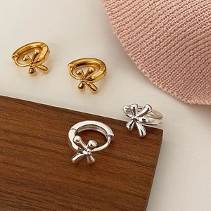 Detailed view of gold and silver bow-knot huggie earrings on a warm decorative setup