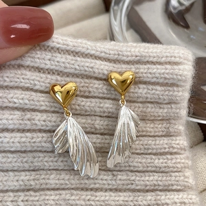 Detail of asymmetric heart wing earrings in gold and silver on knit fabric