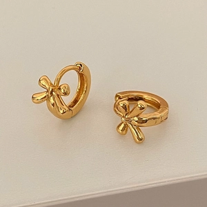 Polished golden bow-knot huggie earrings shown at a 45-degree angle on a beige surface