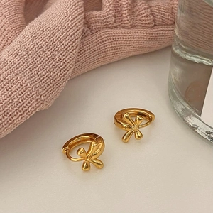 Close-up of elegant gold bow hoop earrings placed on a soft pink knitted fabric