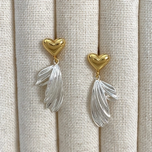 Detailed close-up of asymmetric heart and wing earrings with gold and silver metallic texture