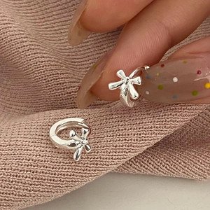 Macro shot of silver bow knot hoop earrings on a soft pink knit texture background