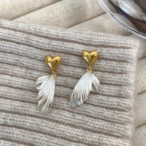 Detail of asymmetrical heart earrings with gold top and silver textured wing-shaped pendant
