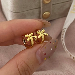 Close-up of golden bow hoop earrings held by hand with warm jewelry box background