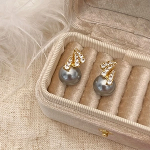 Macro view of gray pearl stud earrings with sparkling zircons in a beige velvet jewelry box