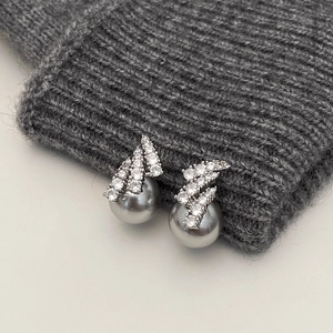 Detail shot of elegant gray pearl earrings with sparkling zircon accents on gray knitwear