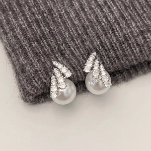 Detail of elegant pearl stud earrings with sparkling zircon feathers on grey knit fabric
