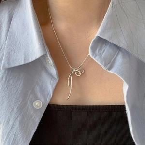 Collier élégant avec pendentif nœud argenté porté par une femme au style minimaliste