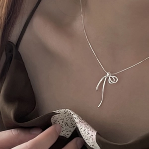 Collier minimaliste avec pendentif nœud en argent sur fond de vêtements en soie