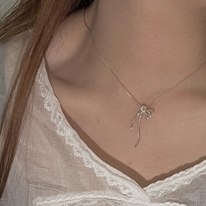 Gros plan d'un collier nœud en argent porté au cou avec un vêtement en dentelle blanche