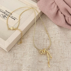 Détail du collier chaîne serpent dorée avec pendentif nœud en ruban et strass brillants
