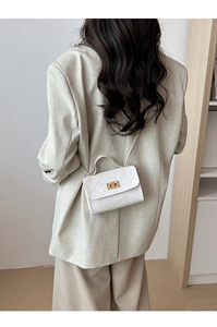 Detalle de bolso bandolera acolchado blanco con cierre de giro dorado y estilo elegante