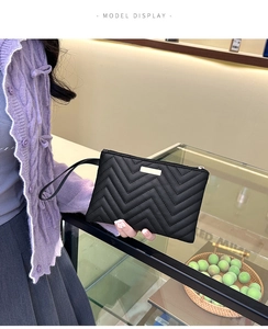 Close-up of black quilted leather clutch with gold metal plaque and wrist strap