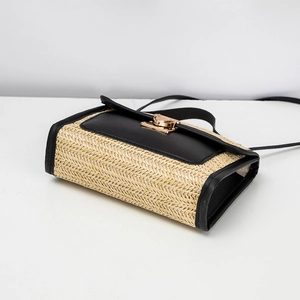 Detail of woven straw handbag featuring black leather trim and a gold twist lock closure