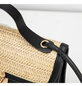 Detail of woven straw texture with black leather handle and gold hardware on a crossbody bag