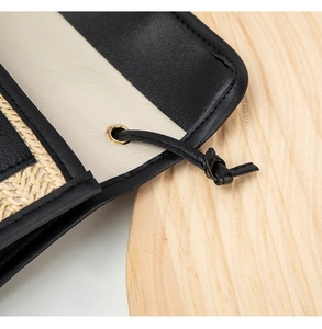 Close-up of woven straw and black leather handbag with gold eyelets and drawstring