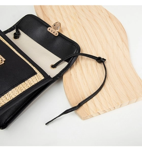 Close-up of woven straw and black textured leather flap bag with gold metal buckle
