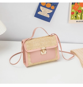 Detail of woven straw and pink leather crossbody bag with a gold clasp on a wooden base