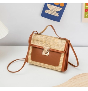 Close-up of a woven straw crossbody bag with brown leather trim and a gold heart lock