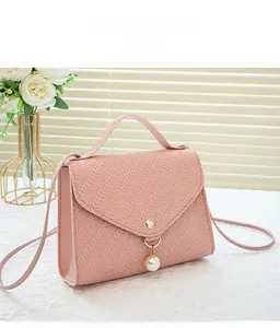 Detail of pink crossbody bag featuring woven texture and elegant white pearl pendant