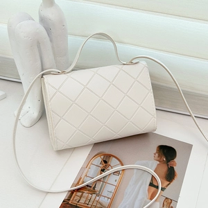 Bolso de mano acolchado crema con asa superior y correa larga sobre un fondo artístico