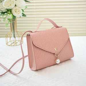 Pink woven texture crossbody bag with pearl pendant and gold hardware on lace background