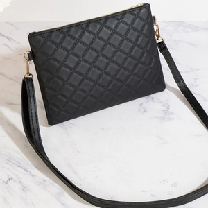 Elegant black quilted crossbody bag with gold hardware on white marble background