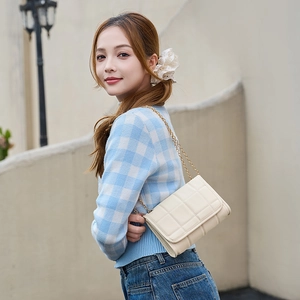 Gesteppte cremefarbene Schultertasche mit goldener Kette getragen von einem Model