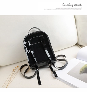 Détail d'un mini sac à dos en cuir verni noir brillant posé sur un canapé en cuir blanc