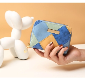 Close-up of geometric patchwork coin purse with matte texture and gold metal logo plate