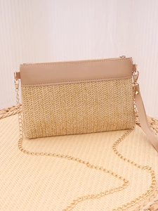 Detail of woven straw crossbody bag with leather trim and gold chain on textured stool